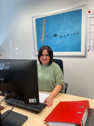 Die Mitarbeiterin sitzt lächelnd vor einem Monitor in ihrem Büro in den Euro-Schulen Aschaffenburg. 