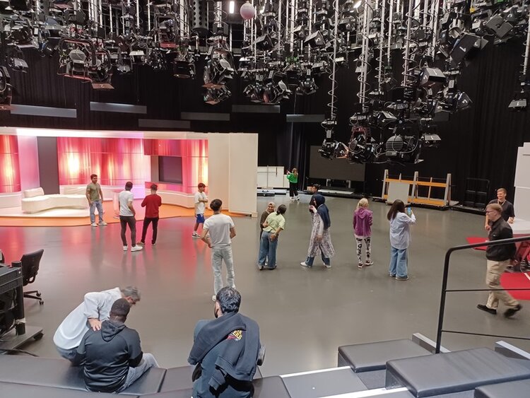 Teilnehmende der Euro-Schulen Mainz sehen sich in einem großen Fernsehstudio um, an der Decke hängen unzählige Scheinwerfer, die Kulisse einer Fernsehsendung ist zu sehen.