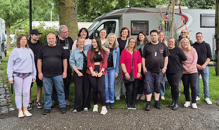 Das Gruppenfoto zeigt die Mitarbeitenden der Euro-Schulen Niederrhein auf dem Campingplatz Düsseldorf, wo sie sich unter einem Baum vor einem Campingmobil positioniert haben.