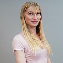 Mitarbeiterin Leonie Beck posiert für ein Porträtfoto und lächelt freundlich in die Kamera. Sie trägt ein nudefarbenes T-Shirt und lange, blonde Haare mit Pony.