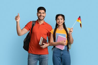 Eine junge Frau mit arabischem Aussehen schwenkt eine Deutschlandflagge, ein junger Mann mit südländischem Teint macht ein "Daumen hoch"-Zeichen. Beide haben Bücher in der Hand und Rücksäcke auf.