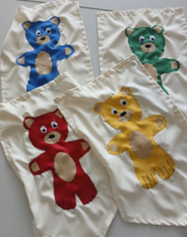 Vier weiße Stoffsäckchen mit aufgenähten Bärenfiguren in Blau, Grün, Rot und Gelb.