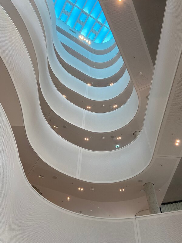 Blick hinauf in ein modern gewölbtes Treppenhaus mit Glasdecke.