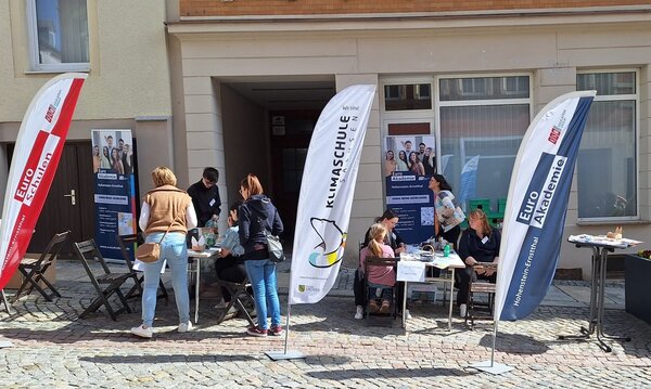 Menschen informieren sich am Stand der Euro Akademie und der Euro-Schulen Hohenstein-Ernstthal beim Frühlingsfest „HOT im Herzen“. Aufsteller und Banner zeigen das Bildungsangebot, während Kinder und Erwachsene an Tischen basteln.