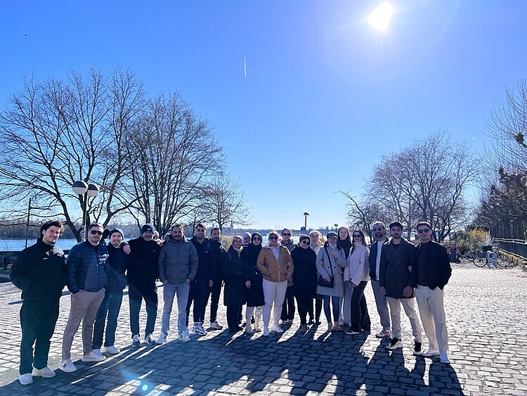 Exkursion des Integrationskurses Die Teilnehmenden des Orientierungskurses posieren bei strahlendem Sonnenschein am Rheinufer für ein Gruppenbild.