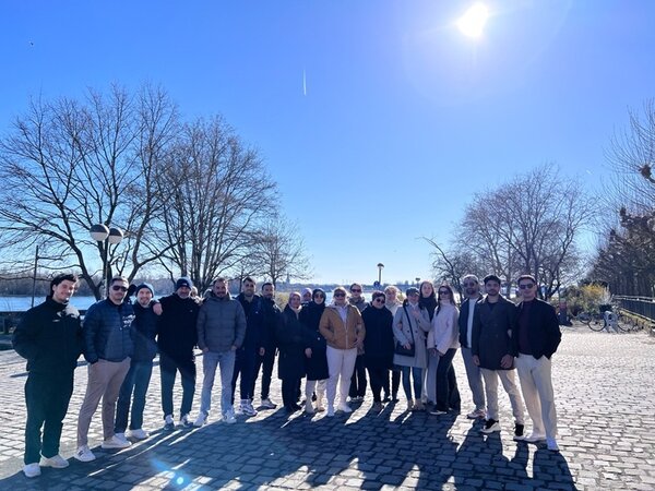 Die Teilnehmenden des Orientierungskurses posieren bei strahlendem Sonnenschein am Rheinufer für ein Gruppenbild.