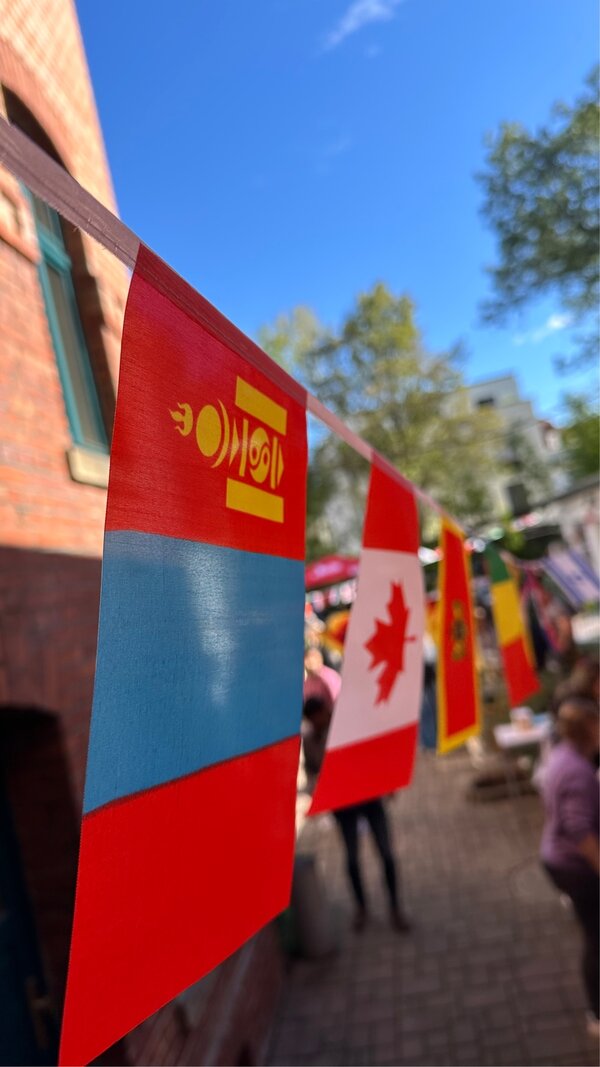 Nahaufnahme einer Girlande mit internationalen Flaggen, im Hintergrund verschwommen das Treiben im Schulhof