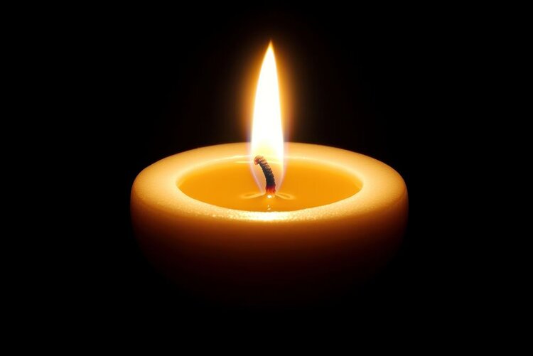 Eine einzelne, helle Kerze befindet sich in der Mitte eines schwarzen Hintergrundes, deren warme gelbe Flamme einen sanften Schein auslöst.
