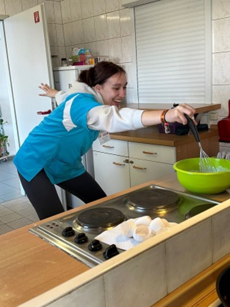 Auszubildende steht am Herd und rührt mit dem Schneebesen in einer grünen Schüssel.