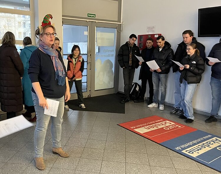 Weihnachtsfeier in Berlin Mitarbeitende stehen im Flur der Schule und machen Lockerungsübungen.