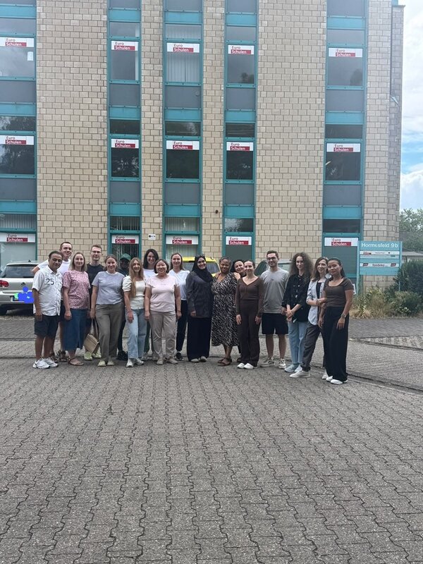 Alle Absolventinnen und Absolventen stehen draußen, vor dem Gebäude der Euro-Schulen Niederrhein, und posieren für ein Gruppenfoto. 