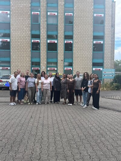 Alle Absolventinnen und Absolventen stehen draußen, vor dem Gebäude der Euro-Schulen Niederrhein, und posieren für ein Gruppenfoto. 