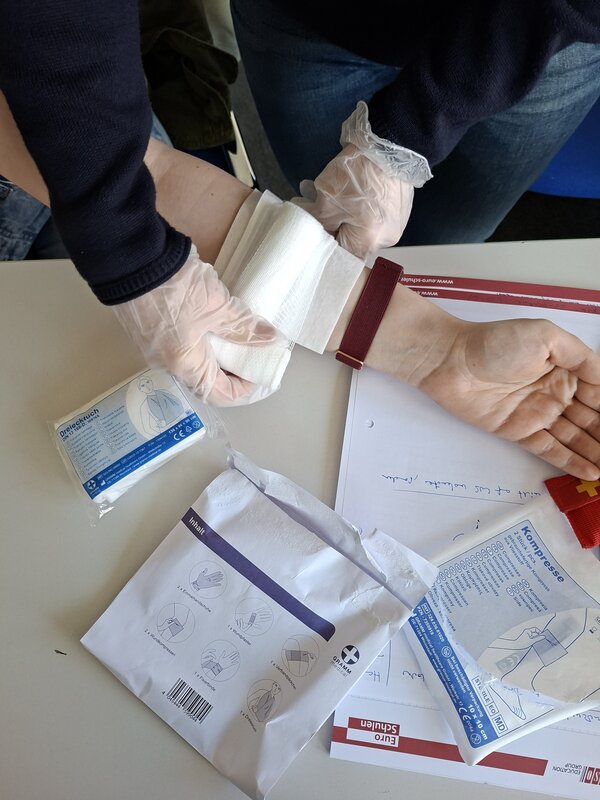 Es ist ein Arm zu sehen, um den jemand mit Latexhandschuhen einen Verband wickelt.