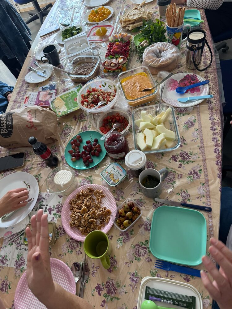 Reich gedeckter Frühstückstisch mit Brot, Eiern, Käse, Gemüse, Obst, Aufstrichen, Salaten, Nüssen und verschiedenen Getränken.