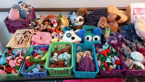 Viele handgemachte Puppen und Kuscheltiere aus Stoff oder Wolle sind in bunten Körben auf einem Tisch ausgebreitet.