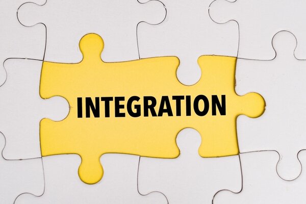 Verschiedene weiße Puzzleteile sind zusammengesetzt und in der Mitte sind zwei dieser Teile orange gefärbt. Auf diesen Teilen steht "Integration" in Schwarz.