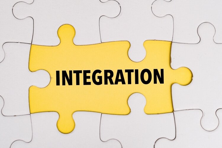 Verschiedene weiße Puzzleteile sind zusammengesetzt und in der Mitte sind zwei dieser Teile orange gefärbt. Auf diesen Teilen steht "Integration" in Schwarz.