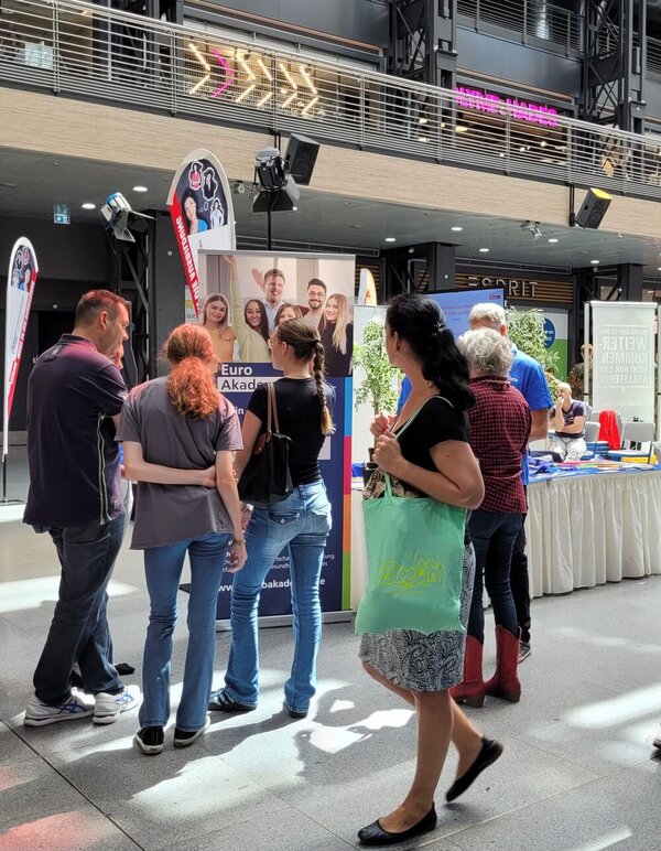 Passant*innen betrachten den Stand der Euro Akademie Berlin.