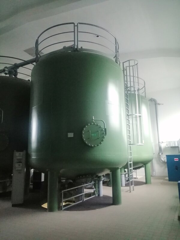 Aufnahme eines großen grünen Behälters, an dem eine Leiter nach oben führt, in einem Maschinenraum des Wasserwerks.