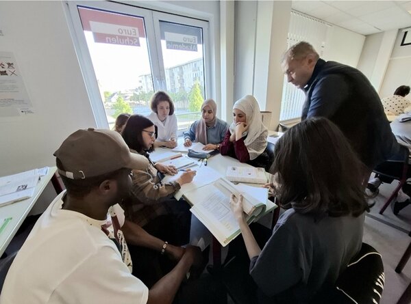 Weibliche und männliche Teilnehmende des B2-Kurses sitzen an einem großen Tisch und arbeiten an ihren gestellten Aufgaben.