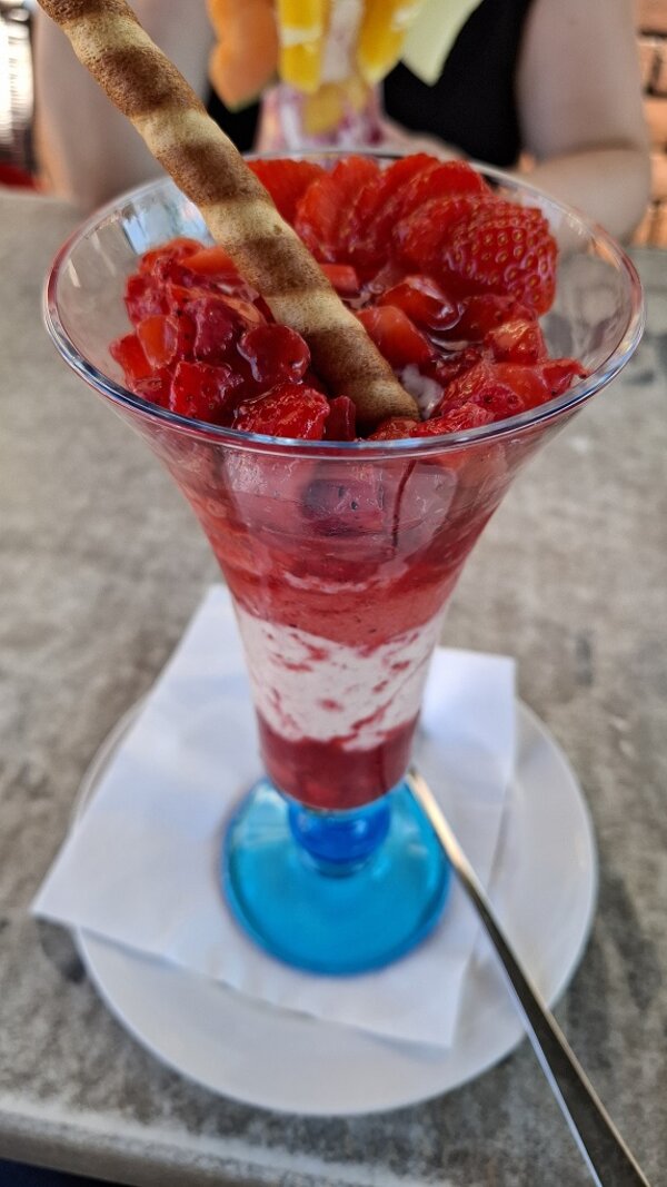 Erdbeerbecher mit Eis, Erdbeersoße, frischen Erdbeeren und einer Waffelrolle in einem hohen Glas.