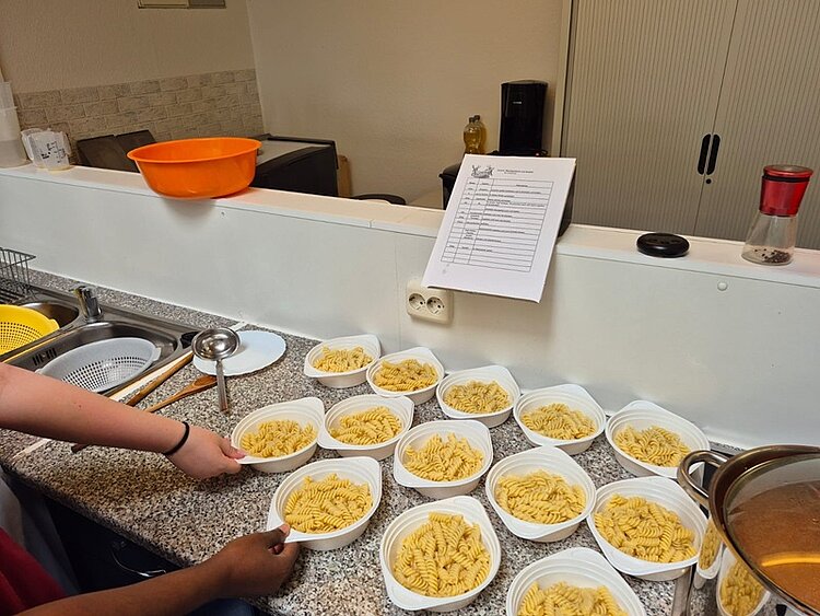 Auf tiefen Einwegtellern angerichtete Spirelli-Nudeln stehen auf der Arbeitsfläche der Küche.