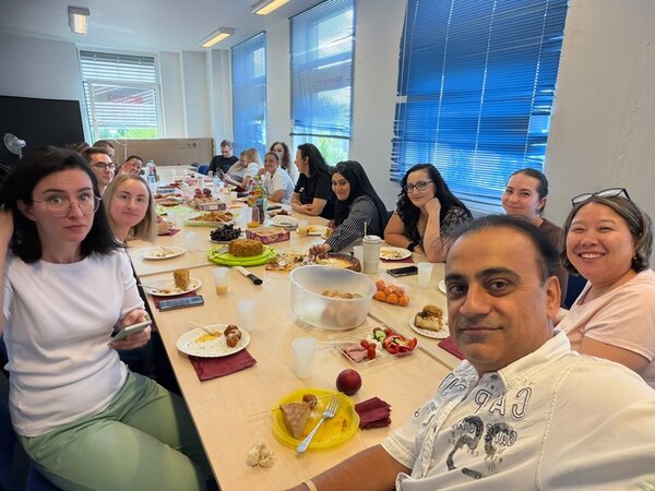 Gruppe von Absolventinnen und Absolventen der Euro-Schulen sitzt gemeinsam an einer langen Tafel in einem hellen Seminarraum und isst verschiedene Speisen in geselliger Runde.