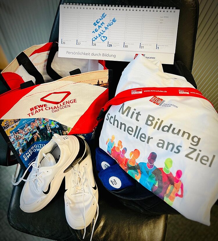 Unsere Teams laufen los – REWE Team Challenge 2025 In einem aufgeklappten Tischkalender der ESO Education Group ist für den 28. Mai 2025 der REWE Team Challenge Lauf 2025 eingetragen, der auf einer Mehrwegtasche mit REWE Team Challenge Aufdruck sowie einem Jute Beutel der ESO Education Group mit Aufschrift "Mit Bildung schneller ans Ziel".