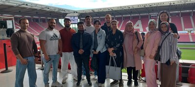 Eine Gruppe von zwölf lächelnden Personen steht zum Gruppenbild in einem Sportstadion.