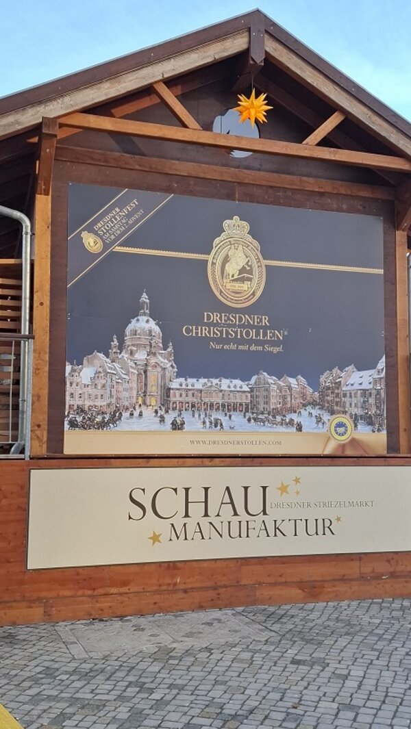 Holzstand mit großem Plakat für den ‚Dresdner Christstollen‘ und der Aufschrift ‚Schau Manufaktur‘ auf dem Dresdner Striezelmarkt.