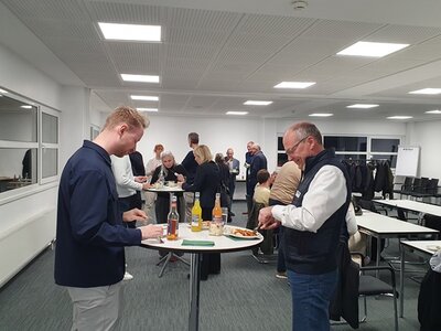 Teilnehmende stehen an Stehtischen und bedienen sich am Buffet.