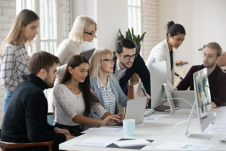 Mehrere Personen arbeiten gemeinsam in einem Büro und gucken zusammen in einen Laptop.