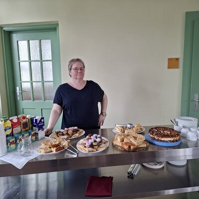 Mitarbeiterin steht am Kuchenbuffet, das sie selbst ausgerichtet hat. 
