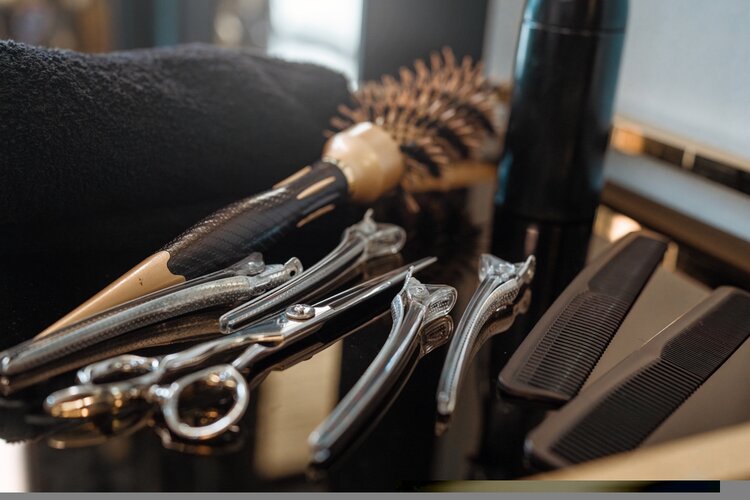 Auf einem schwarz glänzendem Tisch liegen eine Bürste, eine Schere, ein Kamm und Rasierer.