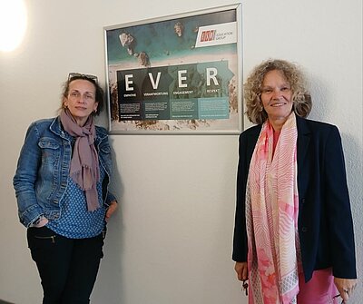 EVER-Plakate zieren Wände der Euro-Schulen Hannover Die Teamleiterin Frau Vuksanovic-Lambert für die Agenturmaßnahme BAli und die Leiterin der Euro-Schulen Hannover Dr. Christiane Ruwoldt stehen neben einem Plakat, auf dem in großen Lettern EVER steht.