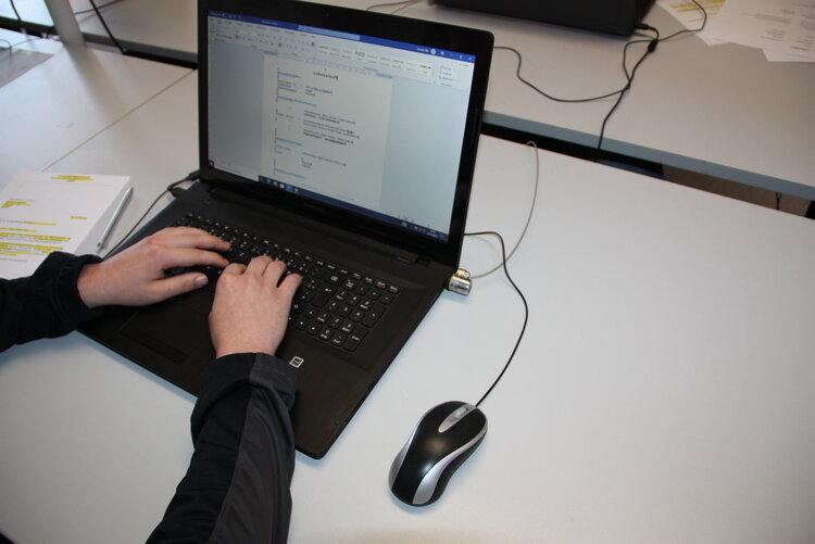 Zwei Hände auf der Tastatur eines Laptops, auf dessen Monitor ein geöffnetes Dokument zu sehen ist. An den Laptop ist eine Maus angeschlossen.