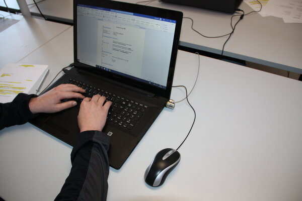 Zwei Hände auf der Tastatur eines Laptops, auf dessen Monitor ein geöffnetes Dokument zu sehen ist. An den Laptop ist eine Maus angeschlossen.