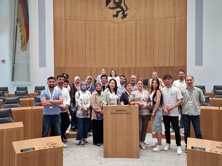 Die weiblichen und männlichen Teilnehmenden des Integrationskurses der Euro-Schulen Mainz stehen gemeinsam hinter dem Rednerpult des Landtages und posieren für ein Gruppenfoto.