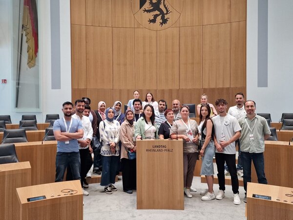 Die weiblichen und männlichen Teilnehmenden des Integrationskurses der Euro-Schulen Mainz stehen gemeinsam hinter dem Rednerpult des Landtages und posieren für ein Gruppenfoto.