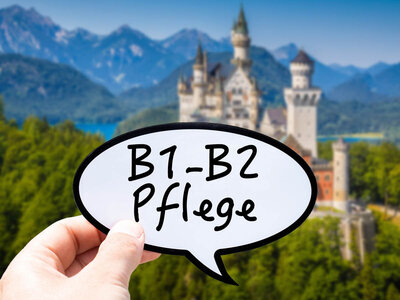 Eine Hand hält eine Sprechblase mit der Aufschrift 'B1-B2 Pflege' in den Vordergrund. Im Hintergrund ist das Schloss Neuschwanstein in den bayerischen Alpen zu sehen. Das Schloss ist von grünen Wäldern und Bergen umgeben, und der Himmel ist klar und blau.