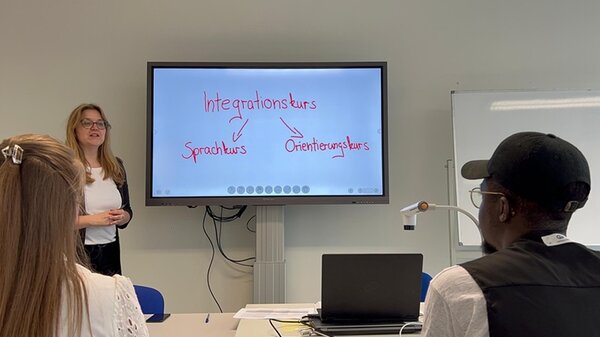 Videodreh an den Euro-Schulen Leipzig. Eine Mitarbeiterin steht vorn an einem Bildschirm und erklärt etwas. 