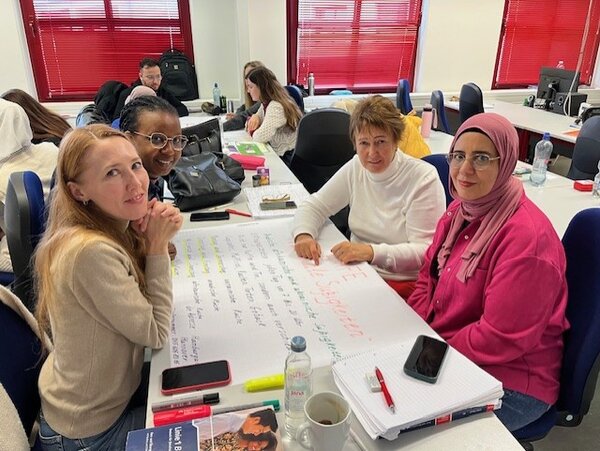 Vier Teilnehmende des Berufssprachkurses sitzen an ihrer Projektarbeit und blicken in die Kamera.