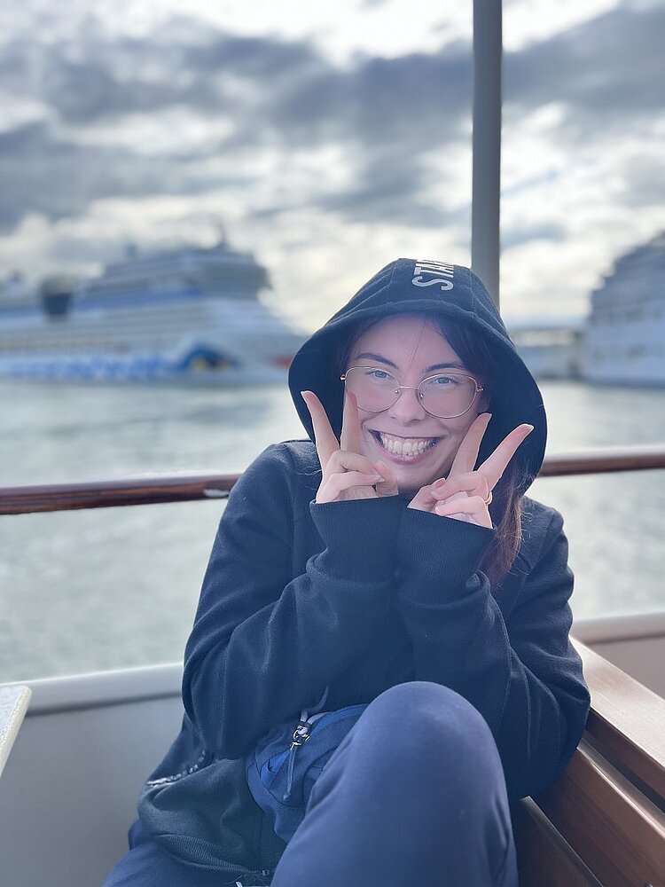 Abschlussfahrt der VK21 an die Ostsee Eine Schülerin zeigt auf einem Boot zwei Peace-Zeichen.