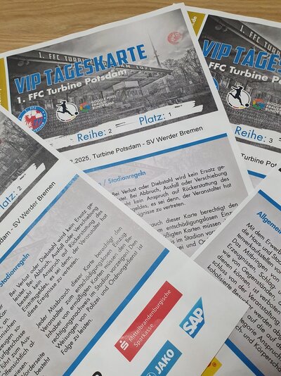 Auf einem Tisch liegen übereinander gefächert vier VIP Tageskarten des 1. FFC Turbine Potsdam, für das Spiel gegen SV Werder Bremen. Auf der Karte ist ein Schwarz-Weiß-Bild des Stadions abgedruckt, darunter ist der Spieltag angegeben und die Stadionregeln sind vermerkt.