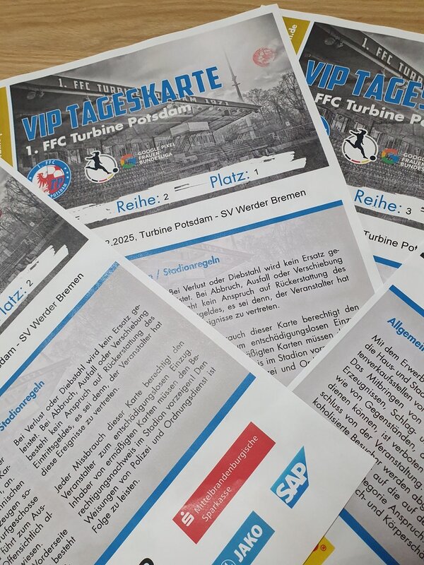 Auf einem Tisch liegen übereinander gefächert vier VIP Tageskarten des 1. FFC Turbine Potsdam, für das Spiel gegen SV Werder Bremen. Auf der Karte ist ein Schwarz-Weiß-Bild des Stadions abgedruckt, darunter ist der Spieltag angegeben und die Stadionregeln sind vermerkt.