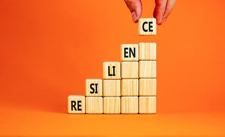 Belastbarkeit im Arbeitsalltag stärken Hölzerne kleine Würfel bilden eine aufsteigene Treppe und das Wort Resilience.