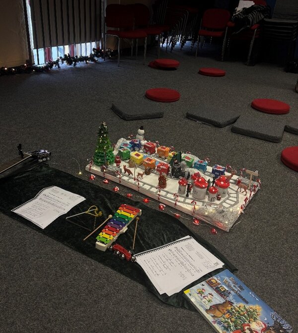 Weihnachtsleseraum mit Teppichboden: In der Mitte stehen eine leuchtende Mini-Winterlandschaft, Xylophon, Triangel und Notenblätter im Stuhlkreis.