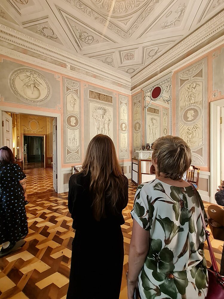 Toller Teamausflug ins Marmorpalais Zwei Personen sind von hinten in einem auffällig verzierten Raum in einem Schloss zu sehen. Sie schauen beide nach oben und betrachten die verzierte Decke.