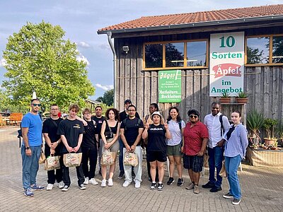 Die Teilnehmerinnen und Teilnehmer des Integrationskurses an den Euro-Schulen Potsdam posieren vor der Obstplantage draußen, bei herrlichem Spätsommerwetter, gemeinsam für ein Gruppenbild