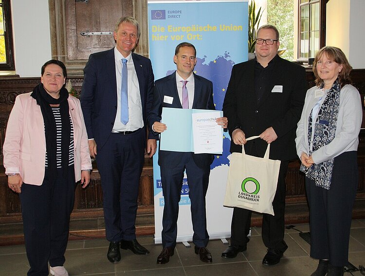 Euro Akademie Oldenburg: weiterhin „die“ Europaschule in Niedersachsen Mehrere Politiker*innen und der Schulleiter Ludwig Knapp haben sich für ein Foto positioniert, dabei wir die Urkunde "Europaschule in Niedersachsen" übergeben. Die Szene spielt sich im Osnabrücker Rathaus ab, hinter den Personen steht ein Rollup, das für die Europäische Union wirbt.
